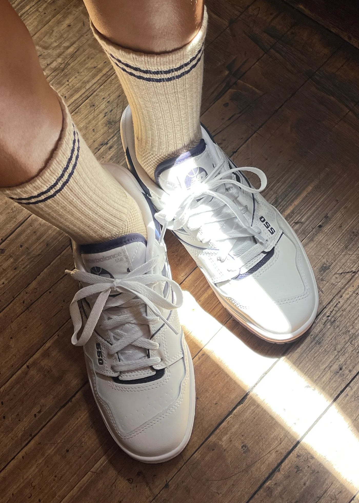 White sneakers with beige socks on a wooden floor