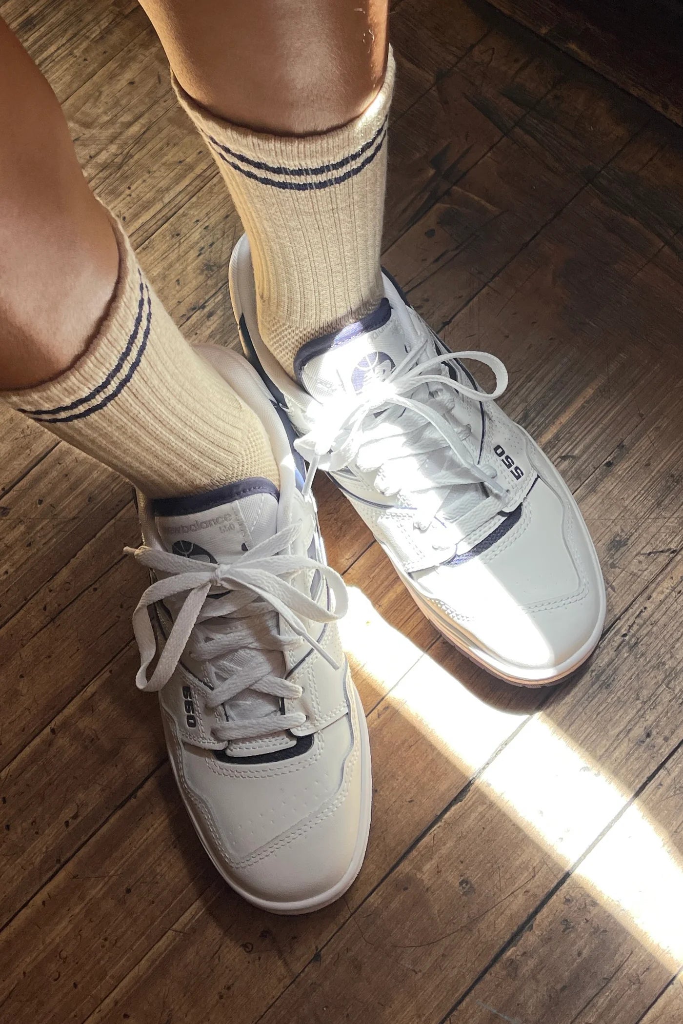 White sneakers with beige socks on a wooden floor