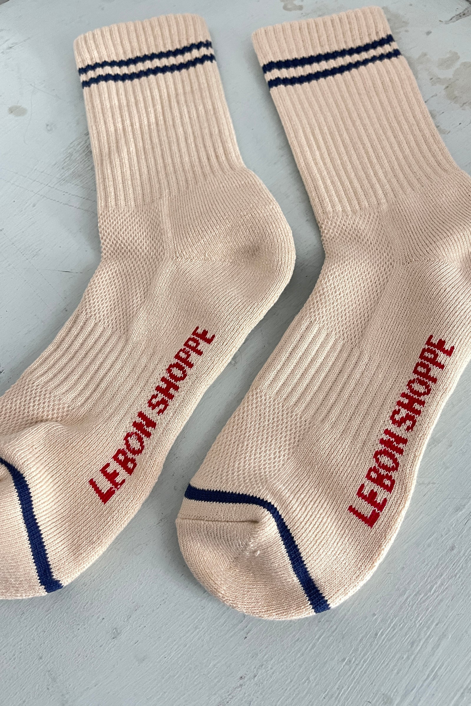 Beige socks with red text 'LEBON SHOPPE' on a light gray background
