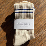 Pair of beige socks with blue stripes on a wooden surface, featuring 'Le Bon Shoppe' label.