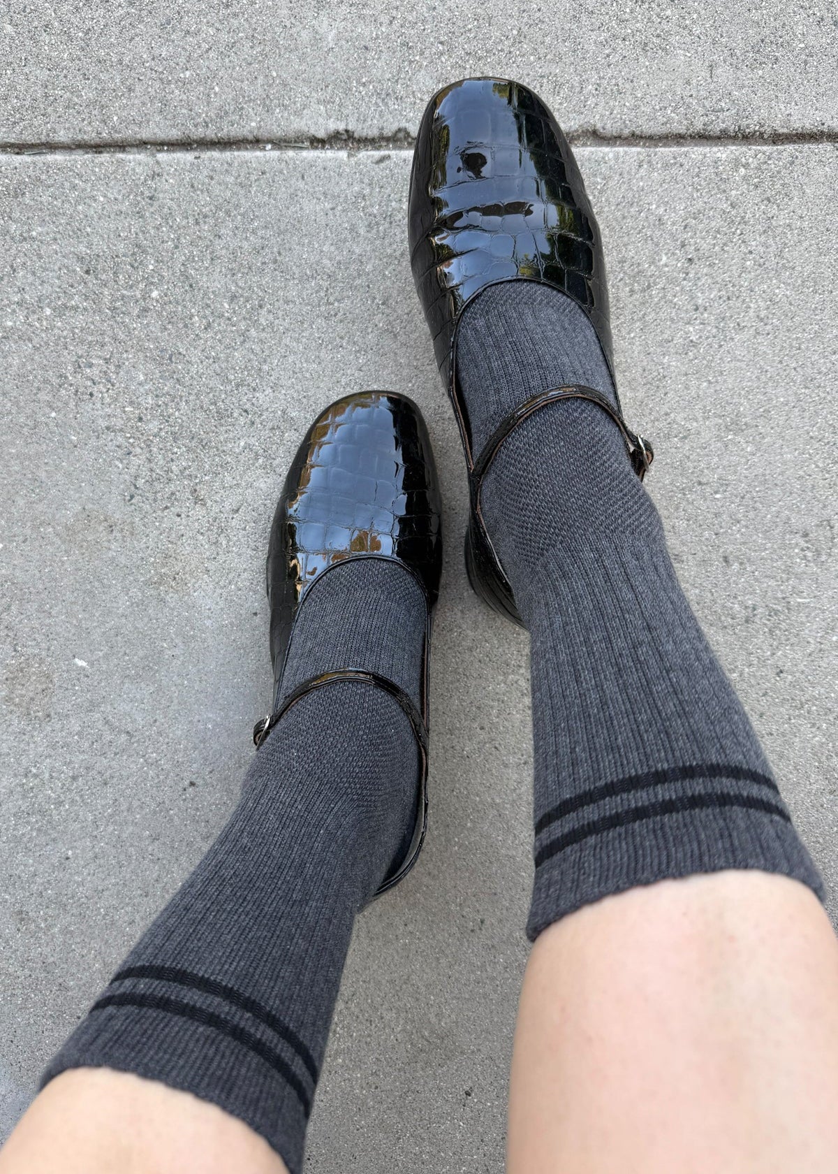 Black shiny shoes and gray socks on a gray pavement background