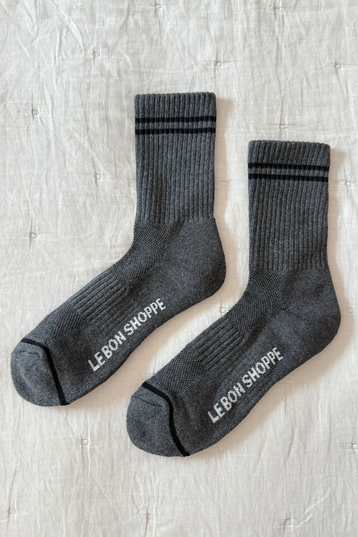 Pair of gray socks with 'Le Bon Shoppe' branding on a light wooden surface