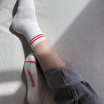 Person wearing white socks with red stripes and grey pants cuffed on a white surface.