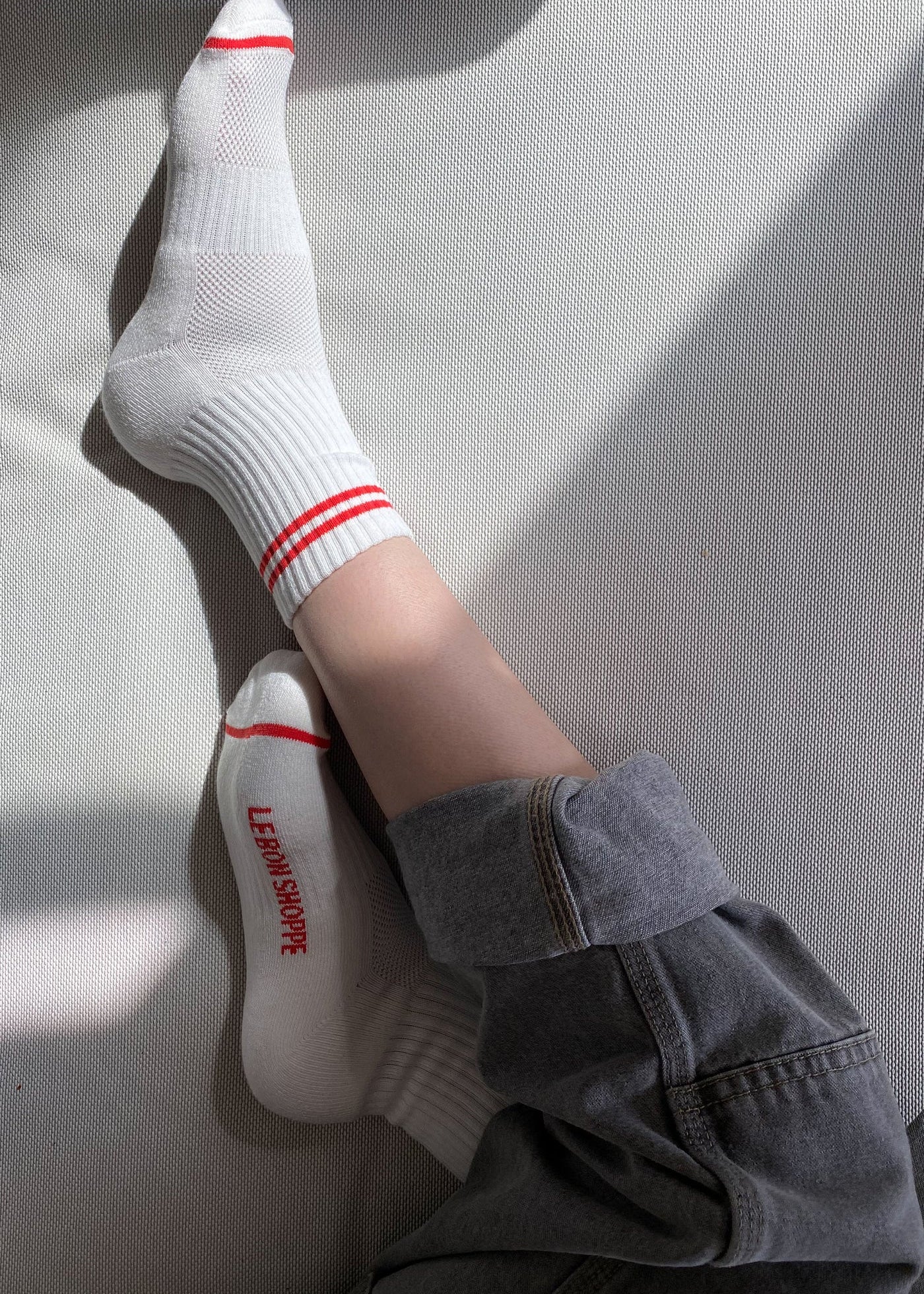 Person wearing white socks with red stripes and grey pants cuffed on a white surface.