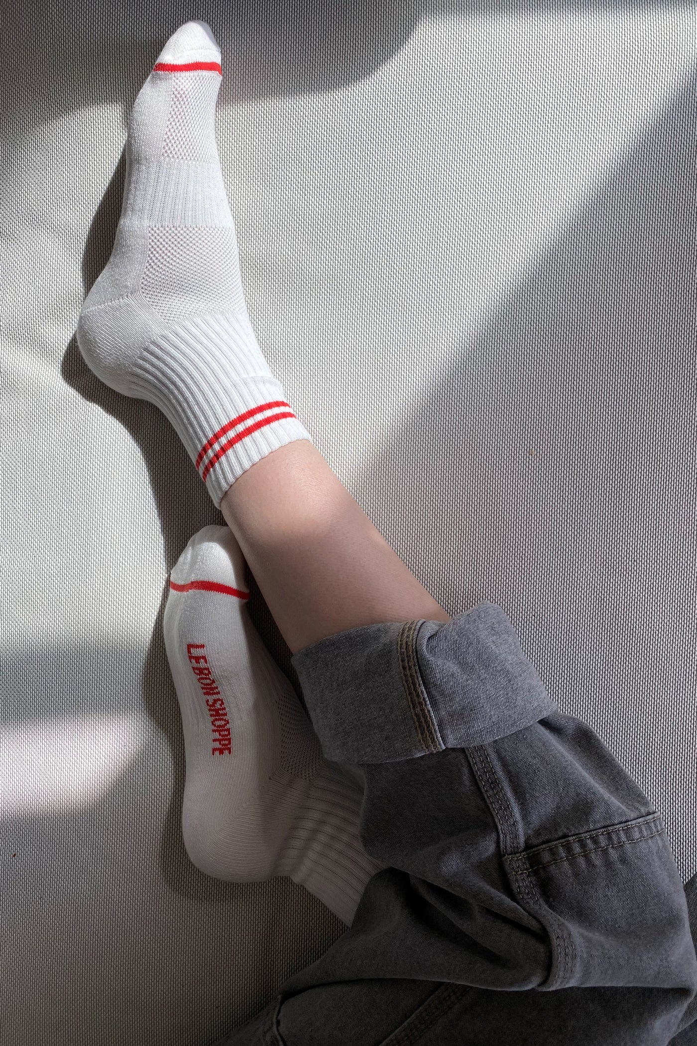 Person wearing white socks with red stripes and grey pants cuffed on a white surface.