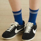 A pair of blue crew socks with a double white stripe, worn with black and white sneakers.