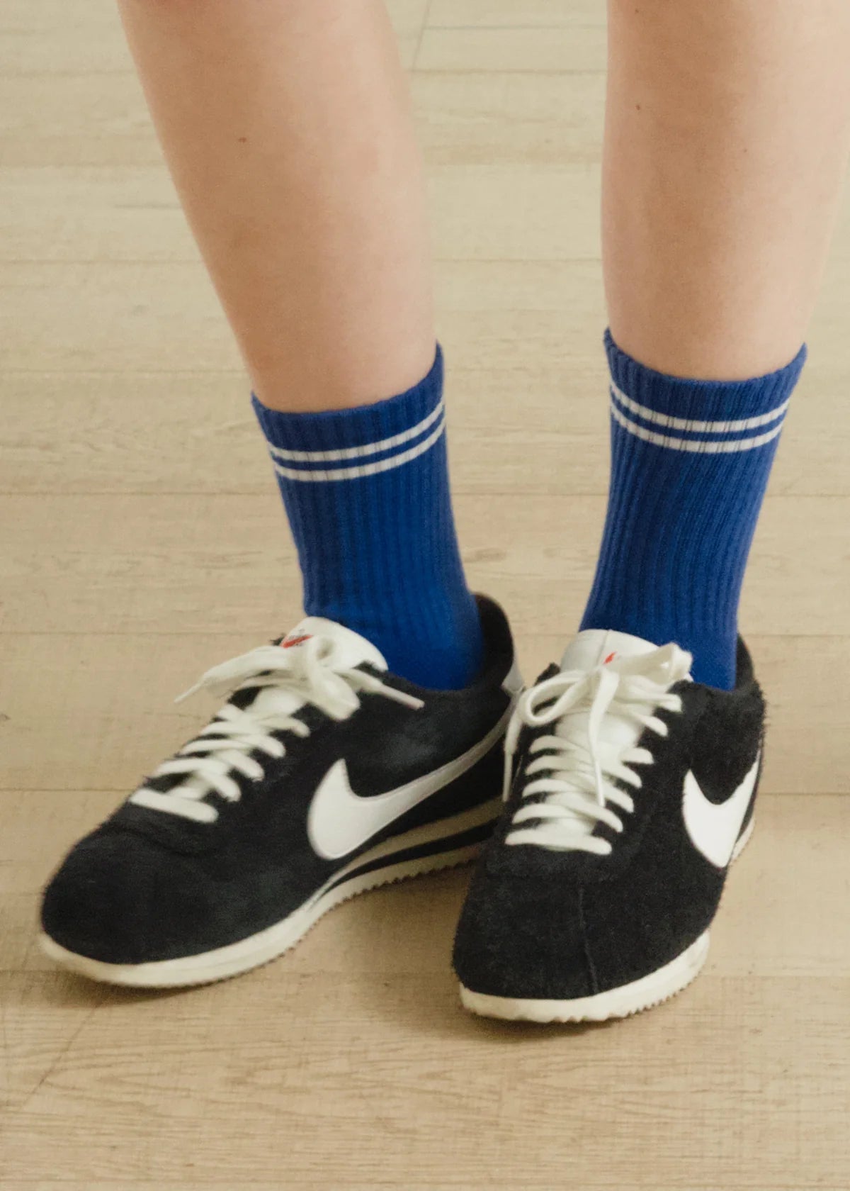 A pair of blue crew socks with a double white stripe, worn with black and white sneakers.