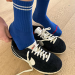 A pair of blue crew socks with a double white stripe, worn with black and white sneakers.