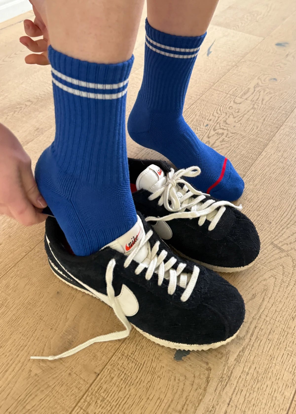 A pair of blue crew socks with a double white stripe, worn with black and white sneakers.