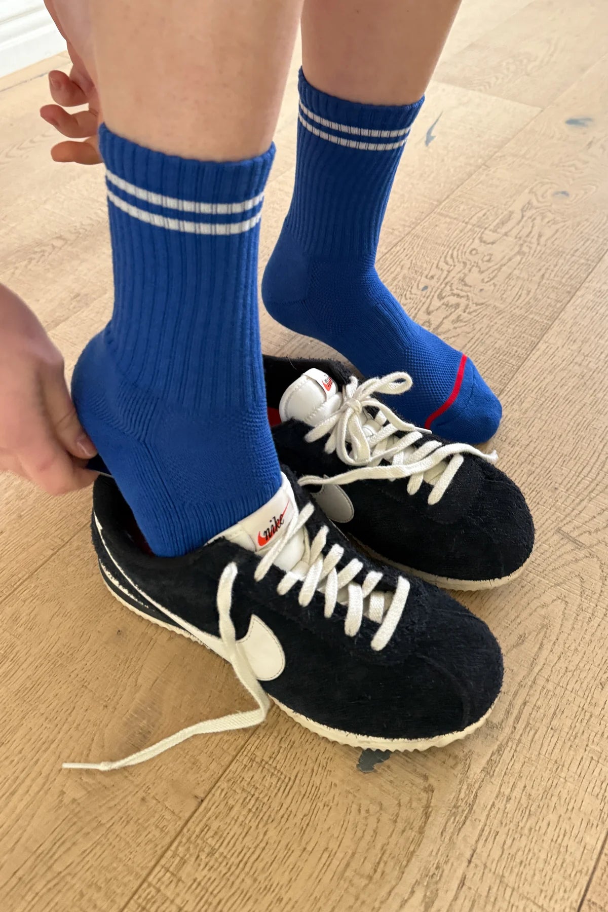 A pair of blue crew socks with a double white stripe, worn with black and white sneakers.
