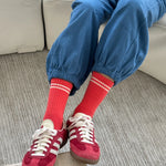 Person wearing red sneakers, red socks with white stripes, and blue pants sitting on a couch.