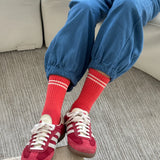 Person wearing red sneakers, red socks with white stripes, and blue pants sitting on a couch.