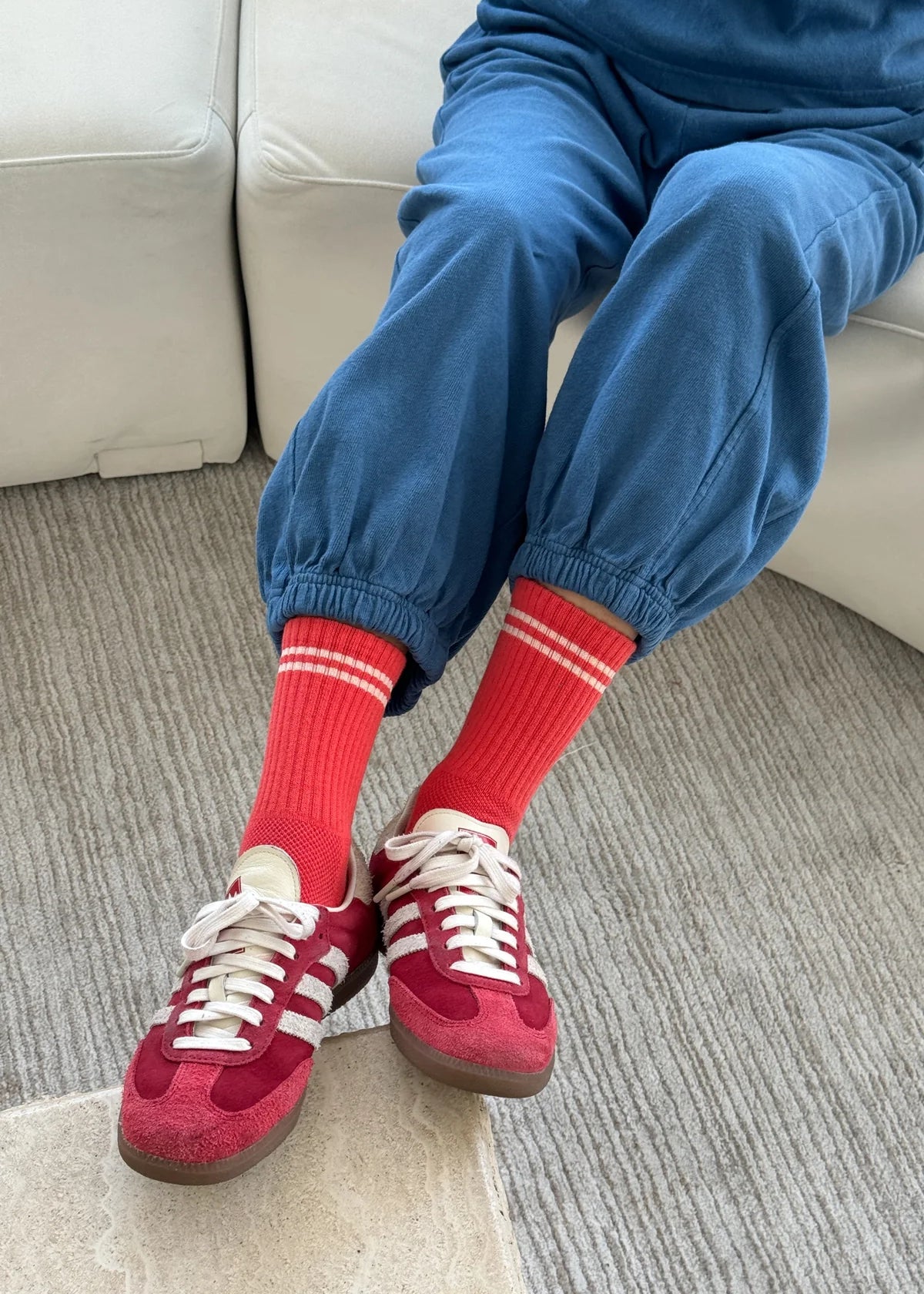 Person wearing red sneakers, red socks with white stripes, and blue pants sitting on a couch.