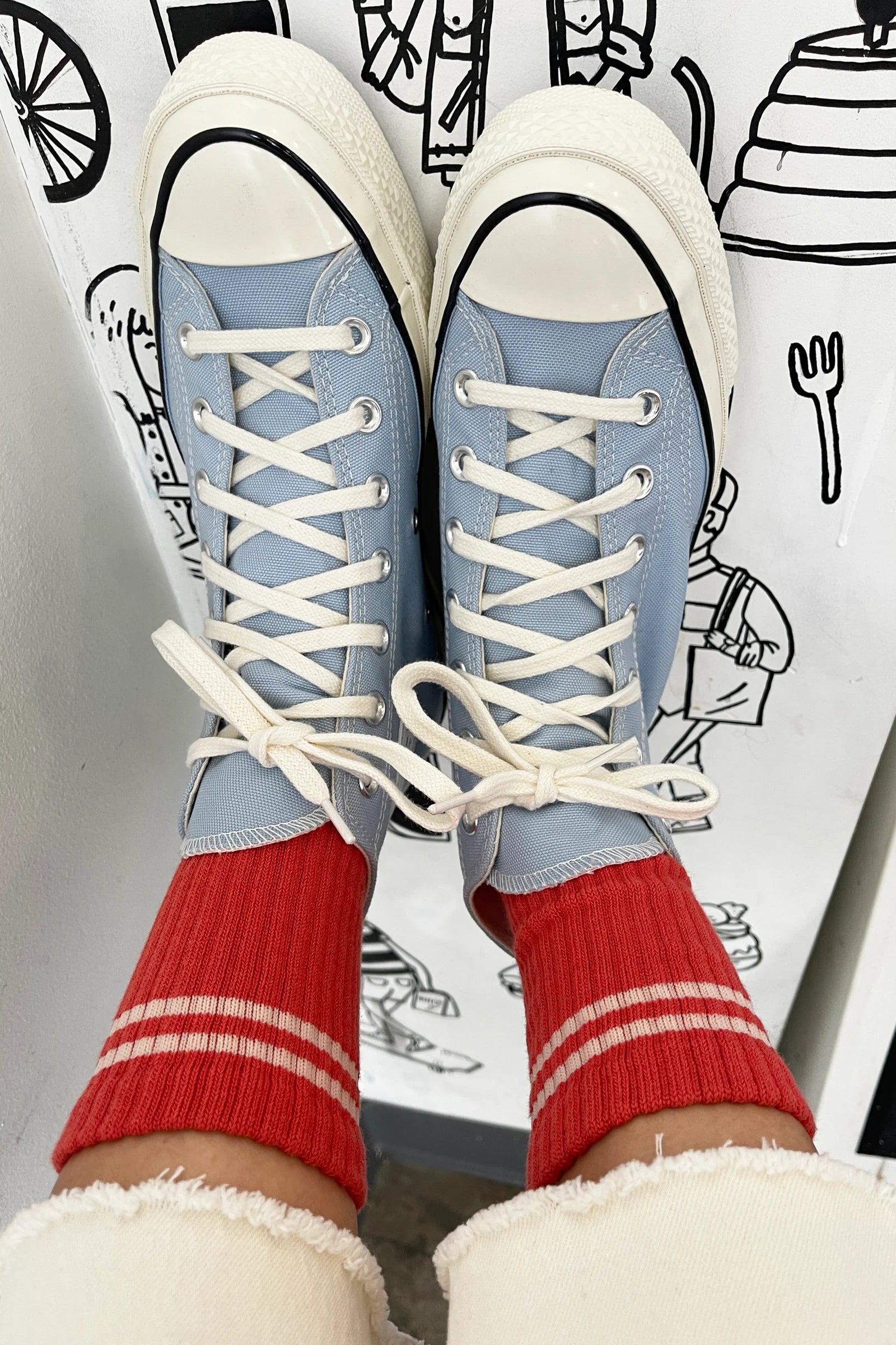 Blue high-top sneakers with white laces worn with red socks against a white background with black line art.