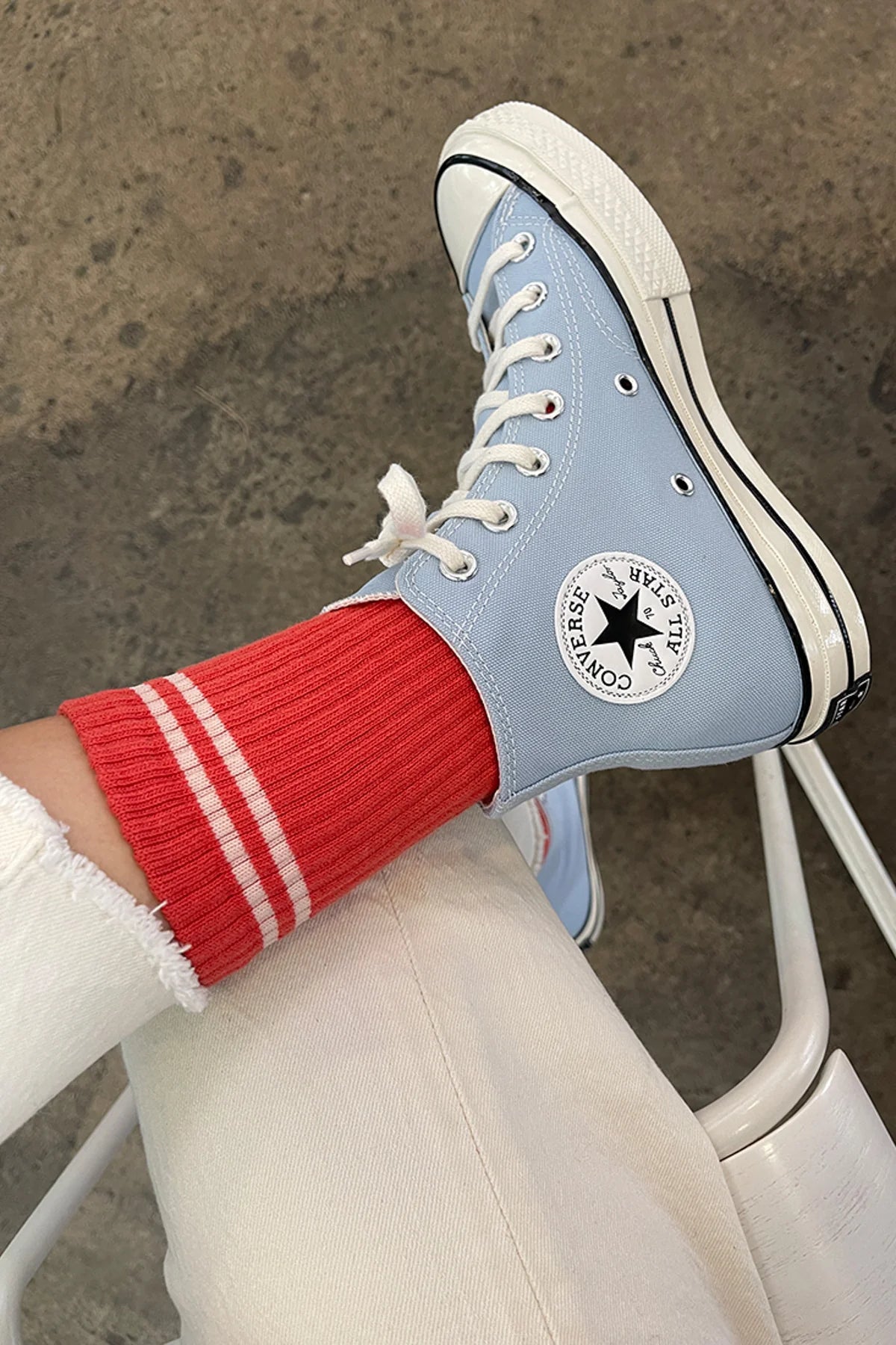 Light blue Converse sneaker with white laces and red sock on a concrete floor.