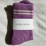 Purple socks with white stripes and a visible label on a gray fabric background