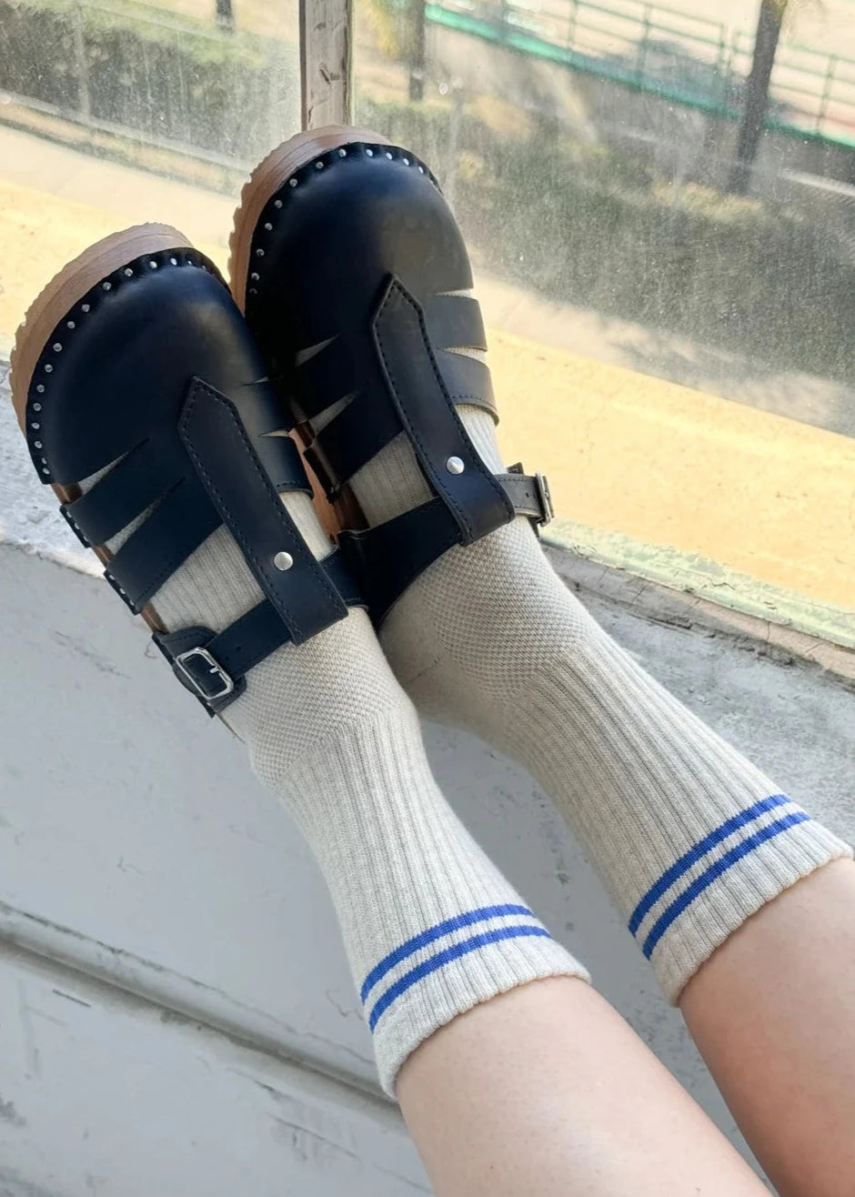 A pair of beige socks with blue stripes on the cuffs, worn with black strap sandals.