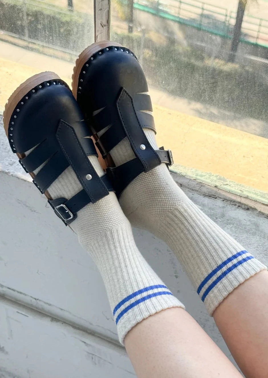 A pair of beige socks with blue stripes on the cuffs, worn with black strap sandals.