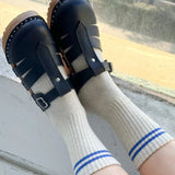 A pair of beige socks with blue stripes on the cuffs, worn with black strap sandals.