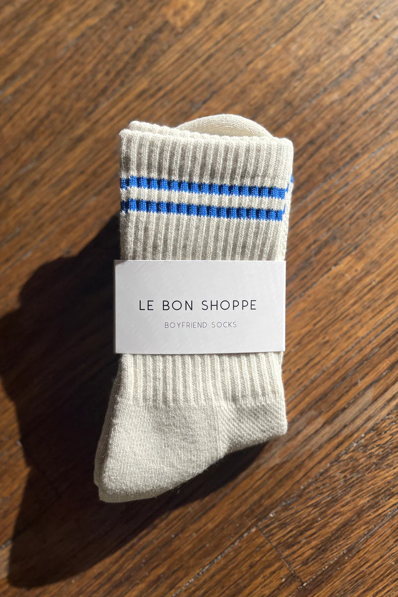 Oatmeal socks with blue stripes in Le Bon Shoppe Packaging on a wood floor.