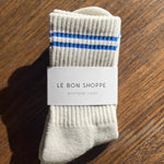 Oatmeal socks with blue stripes in Le Bon Shoppe Packaging on a wood floor.