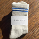 Oatmeal socks with blue stripes in Le Bon Shoppe Packaging on a wood floor.