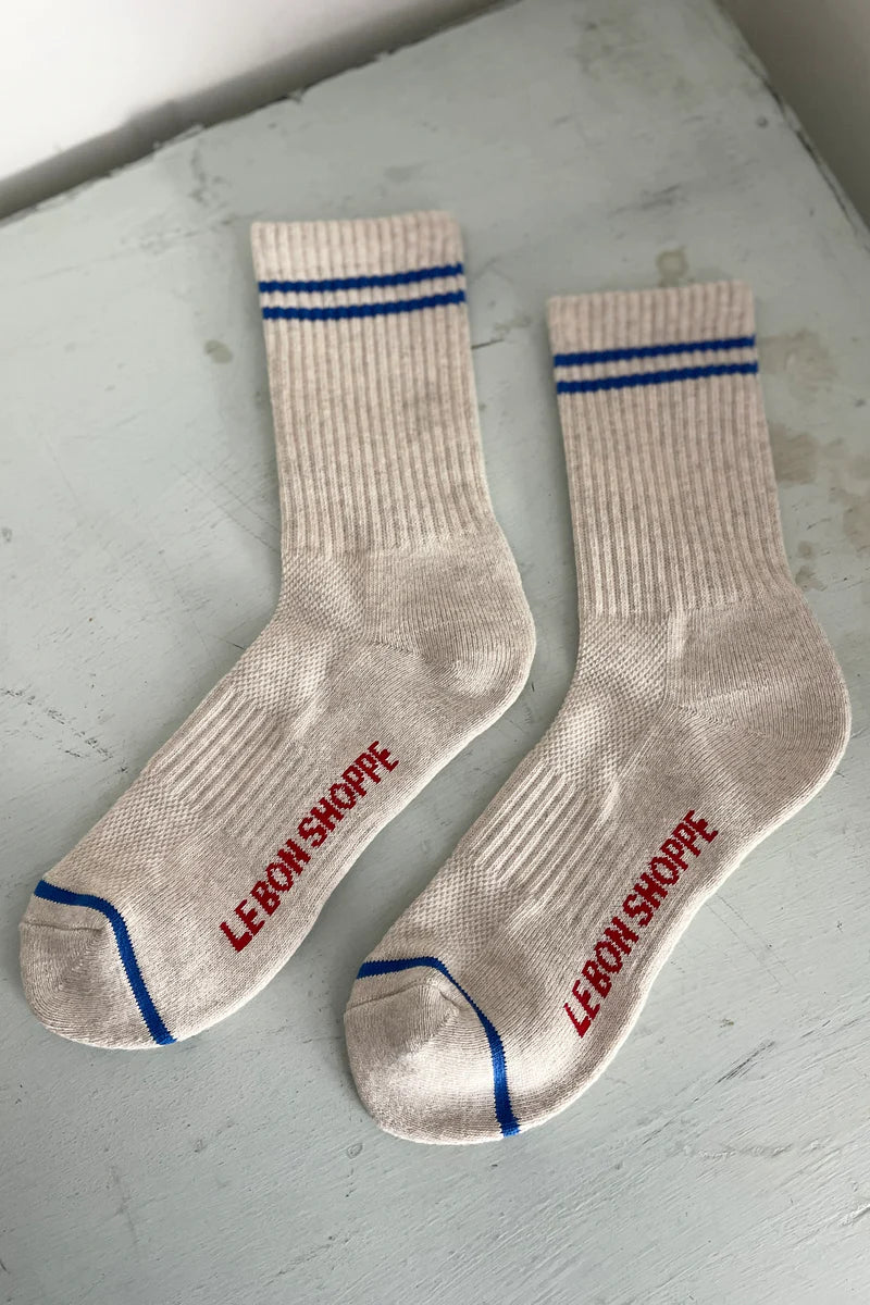 Oatmeal socks with blue stripes in Le Bon Shoppe Packaging on a painted floor.