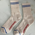 Oatmeal socks with blue stripes in Le Bon Shoppe Packaging on a painted floor.