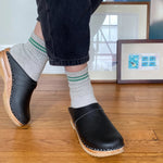 Person wearing black clogs and striped socks on a wooden floor.