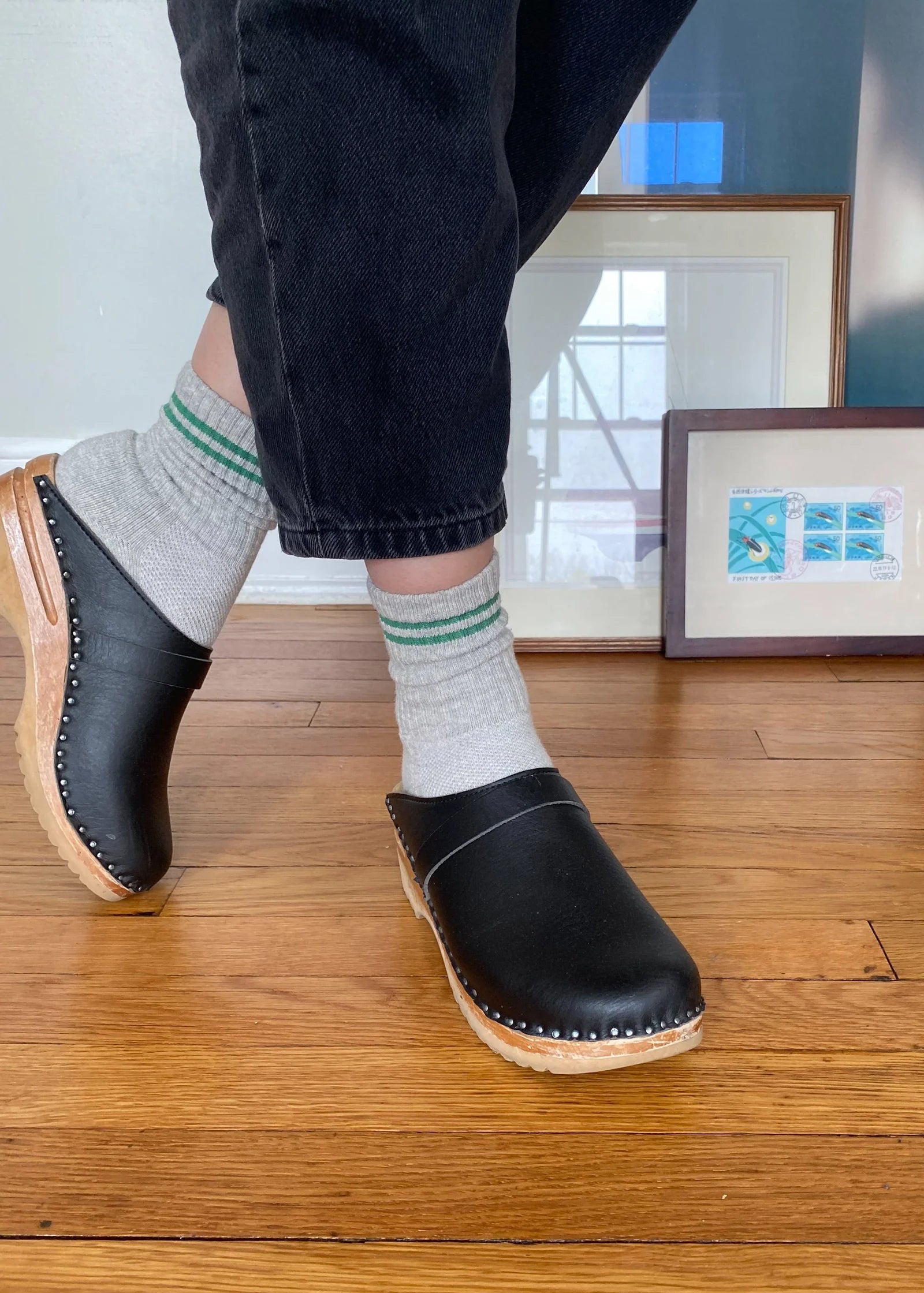 Person wearing black clogs and striped socks on a wooden floor.