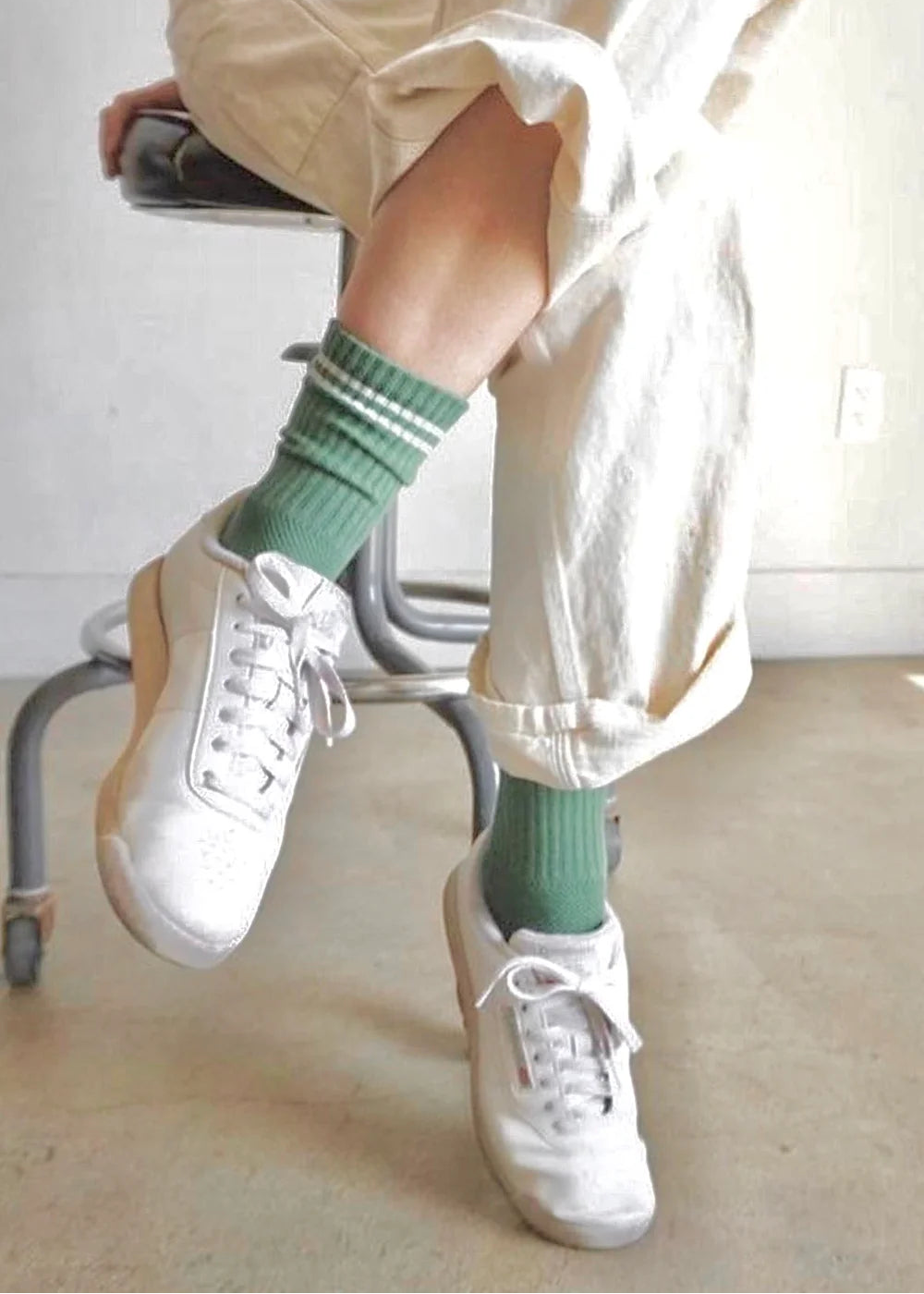 Person wearing white sneakers and green socks sitting on a chair.