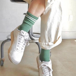 Person wearing white sneakers and green socks sitting on a chair.