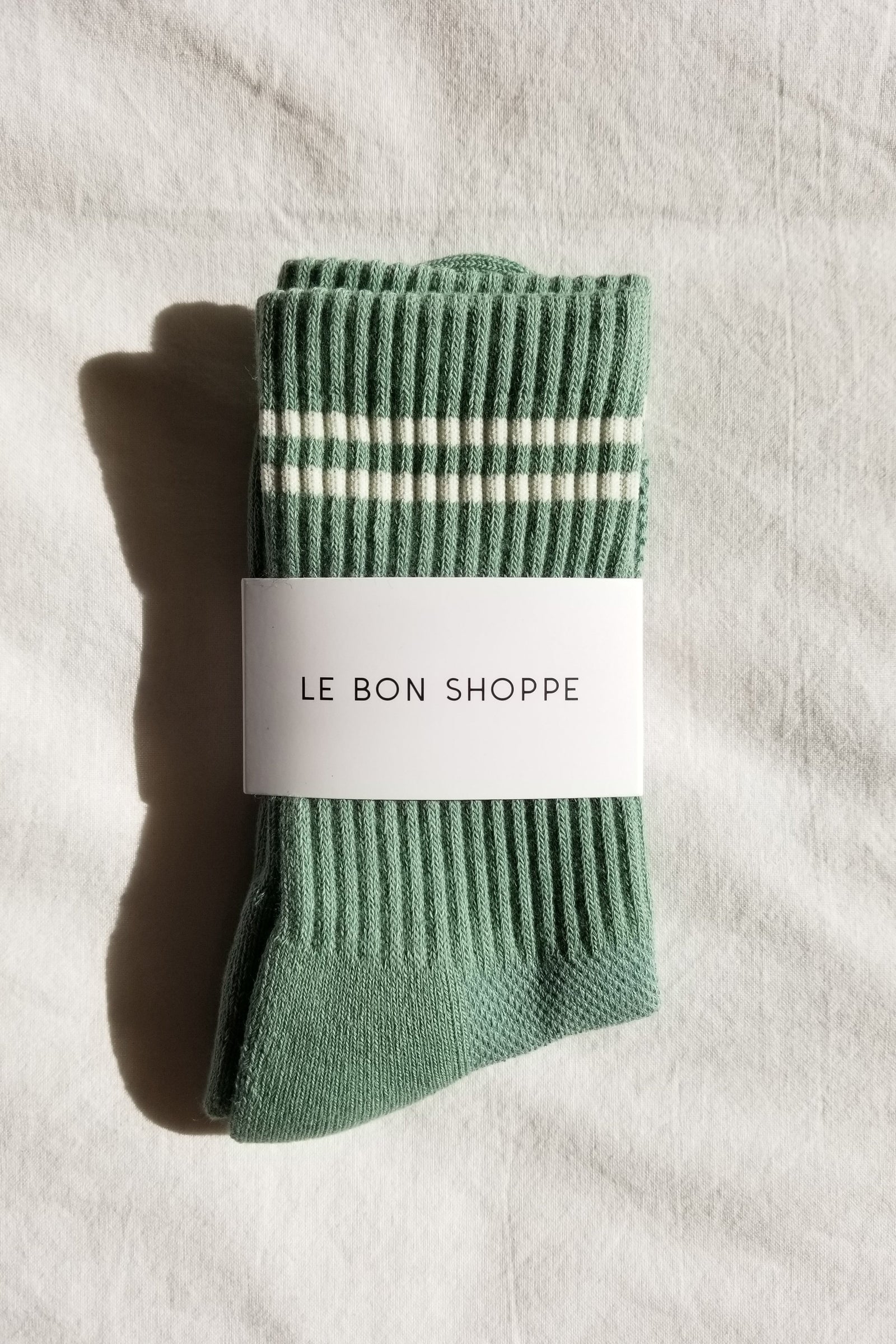 Green sock with white stripes and 'Le Bon Shoppe' label on a light background