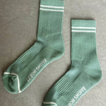 Two green socks with white stripes and 'Le Bon Shoppe' branding on a gray surface.