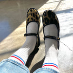 Person wearing leopard print shoes, white socks with red and blue stripes, and blue jeans on a concrete floor.
