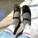 Person wearing leopard print shoes, white socks with red and blue stripes, and blue jeans on a concrete floor.