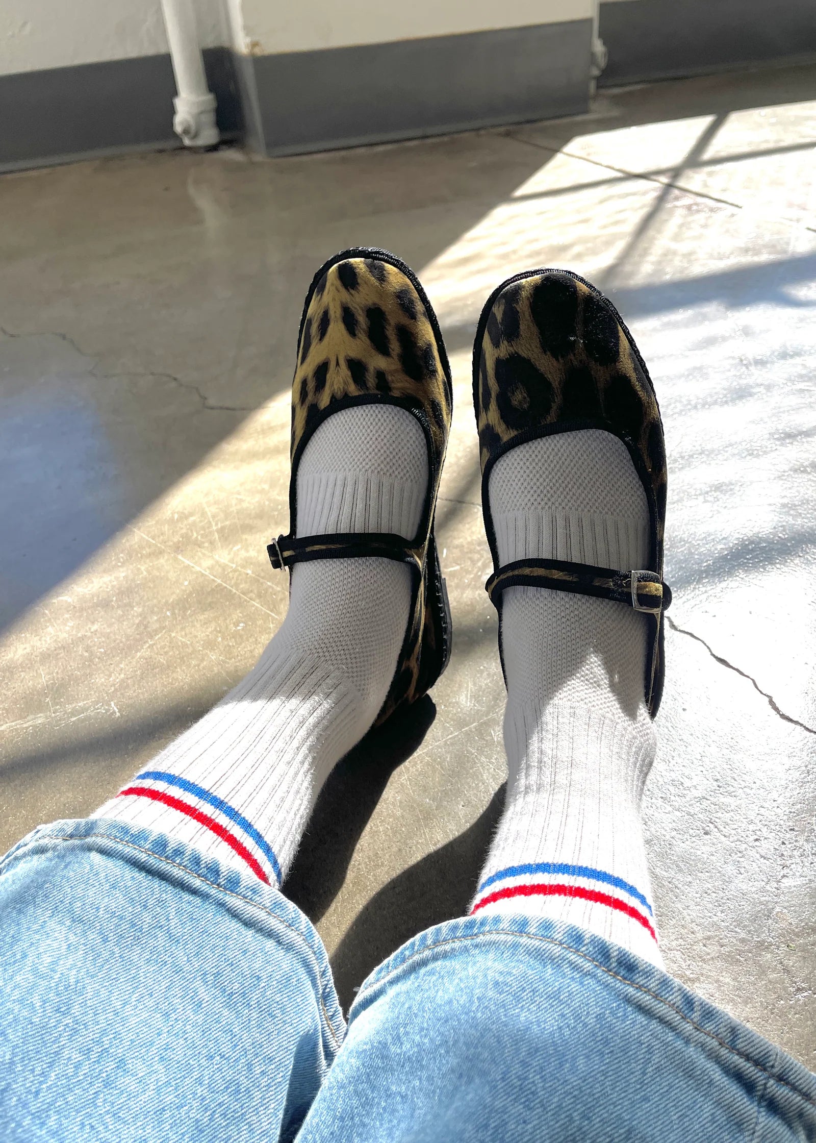 Person wearing leopard print shoes, white socks with red and blue stripes, and blue jeans on a concrete floor.
