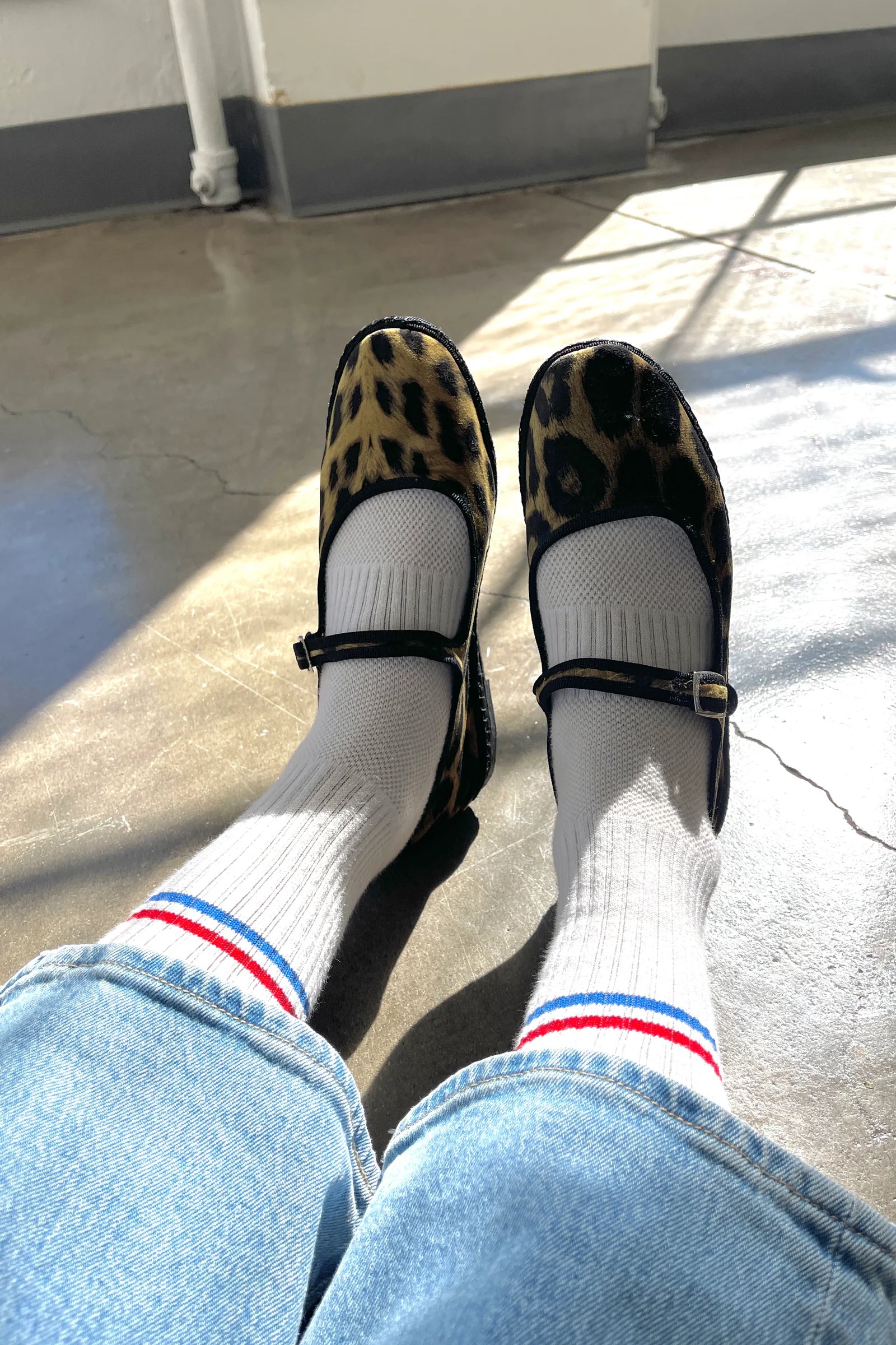 Person wearing leopard print shoes, white socks with red and blue stripes, and blue jeans on a concrete floor.