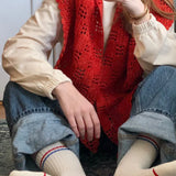 Person wearing a red knitted vest and white socks with text, sitting on a carpeted floor.