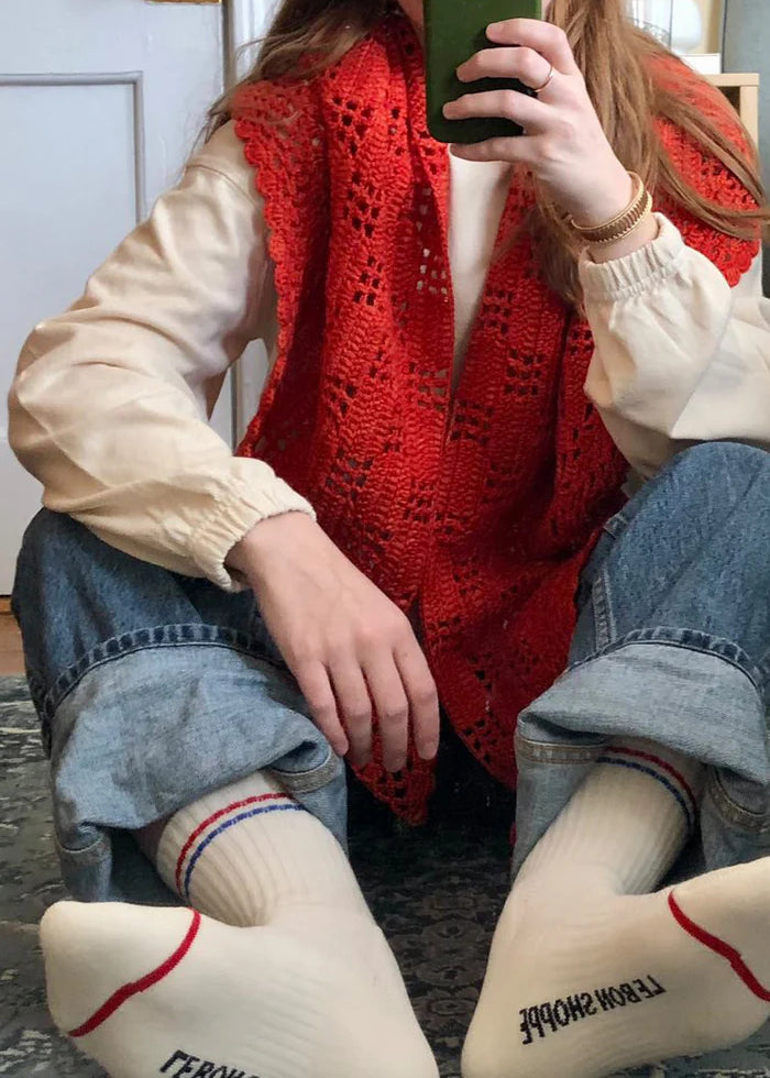 Person wearing a red knitted vest and white socks with text, sitting on a carpeted floor.