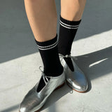 Person wearing black socks with white stripes and silver shoes on a concrete surface