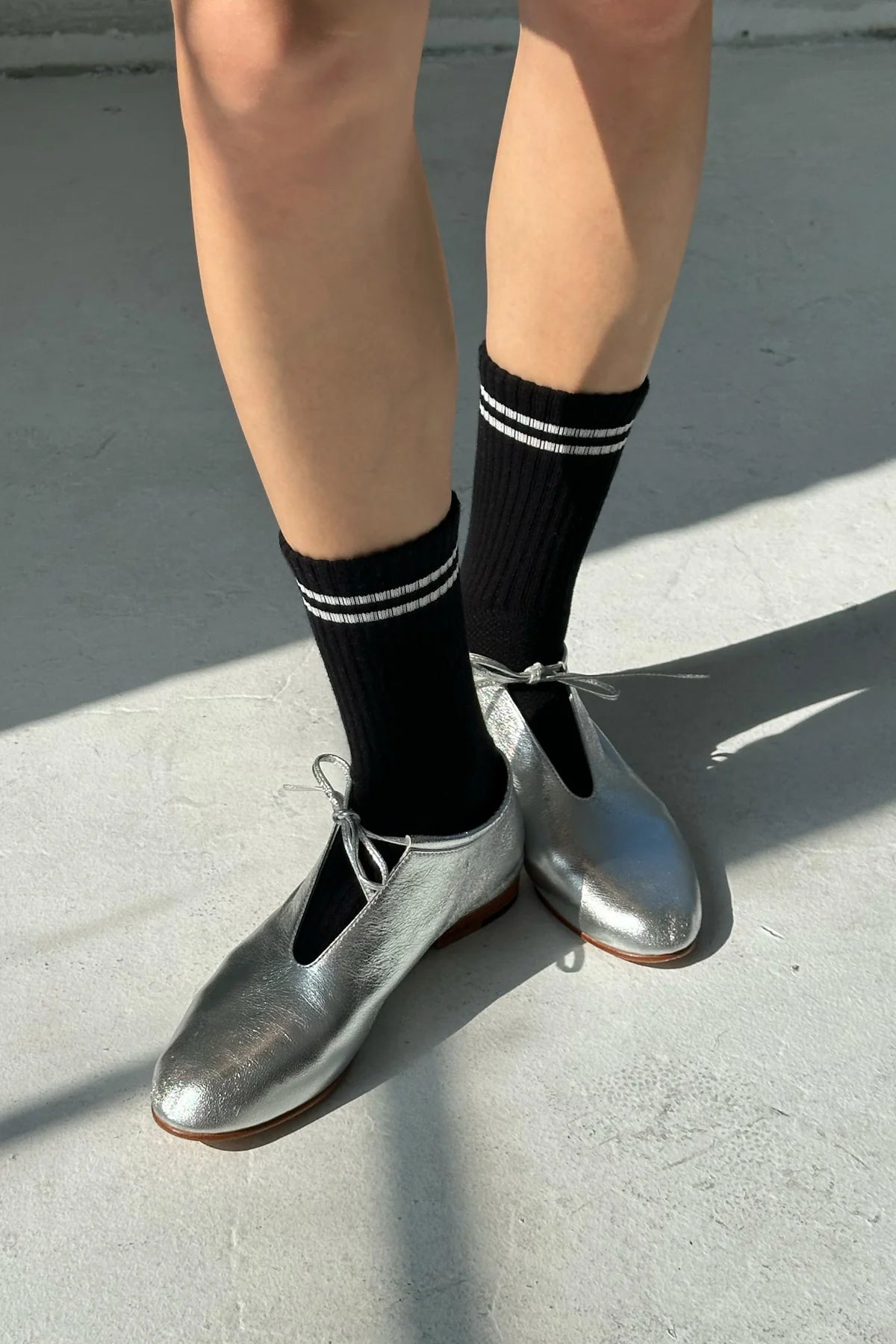 Person wearing black socks with white stripes and silver shoes on a concrete surface