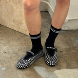 Black studded flats worn with black socks on a concrete floor.