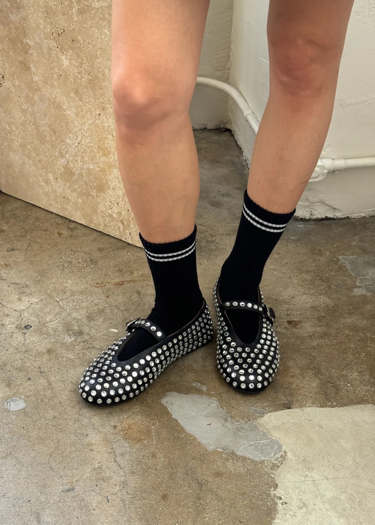 Black studded flats worn with black socks on a concrete floor.