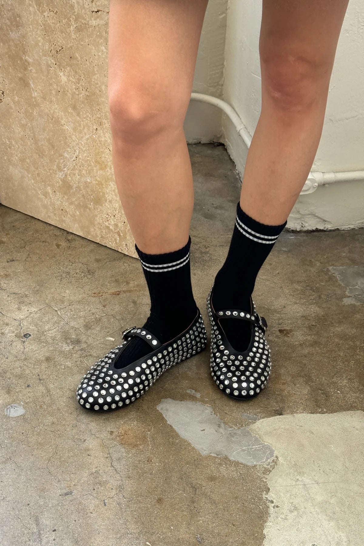 Black studded flats worn with black socks on a concrete floor.