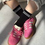 Pink sneakers with white stripes worn on a light gray surface