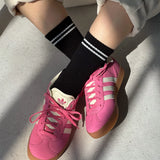 Pink sneakers with white stripes worn on a light gray surface