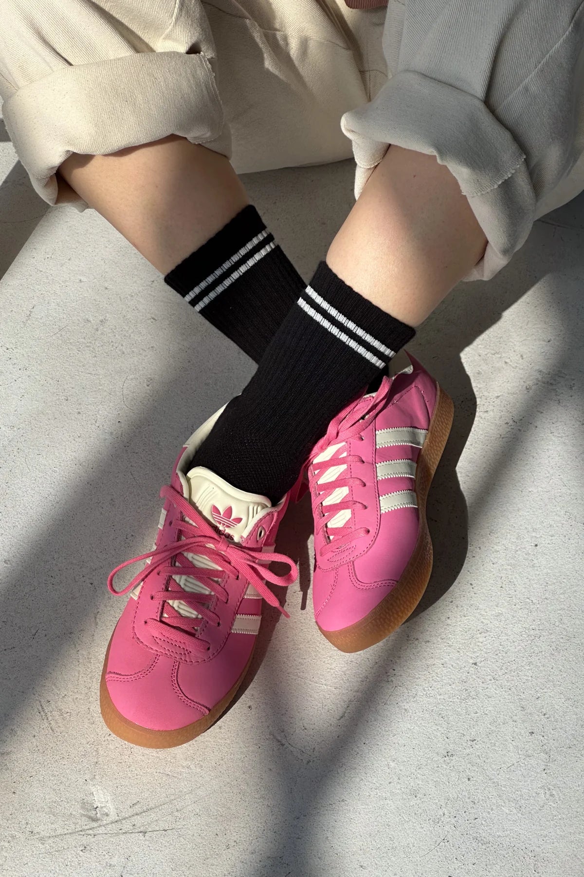 Pink sneakers with white stripes worn on a light gray surface