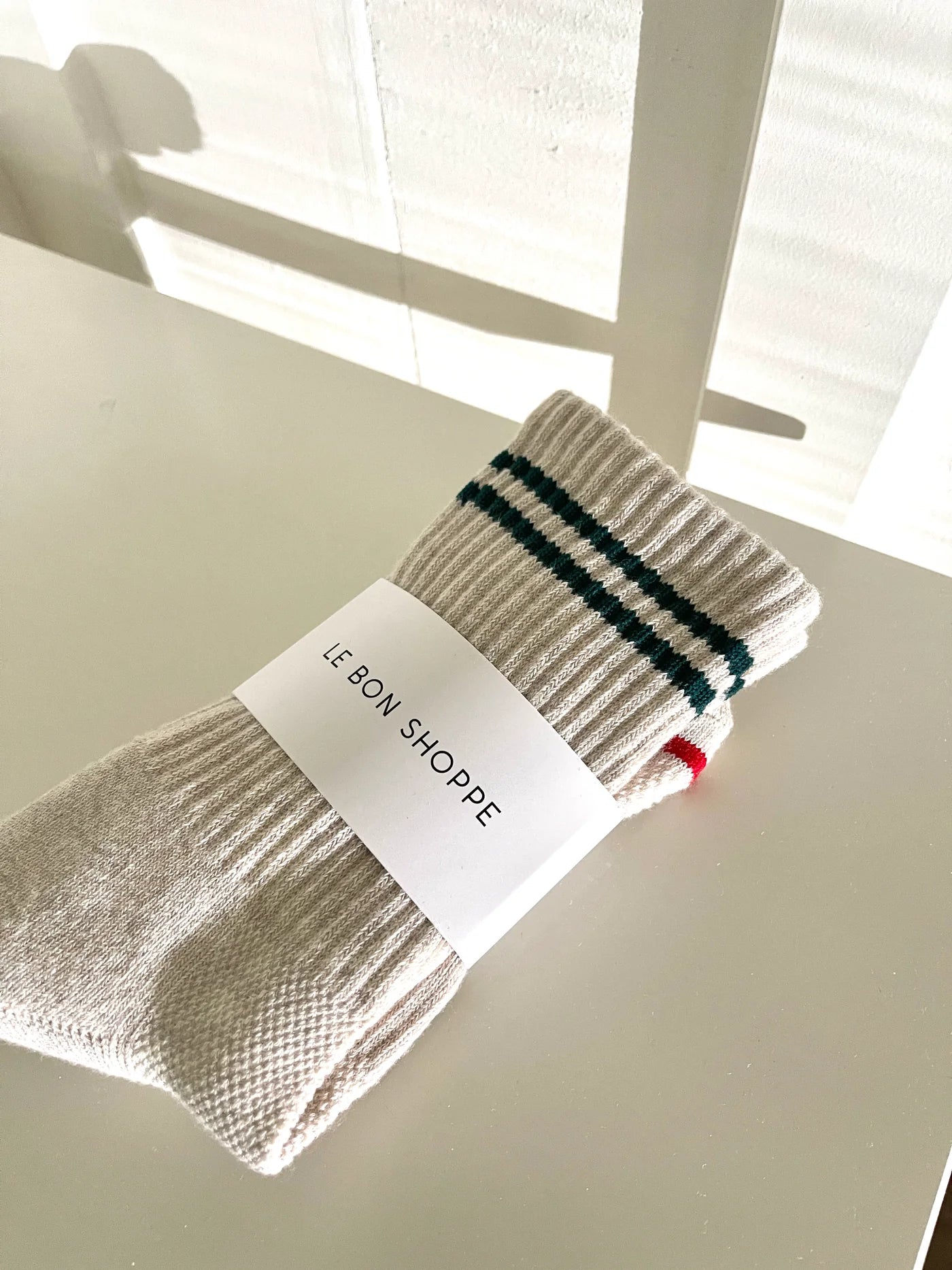 Cream color socks with green stripes in Le Bon Shoppe packaging.