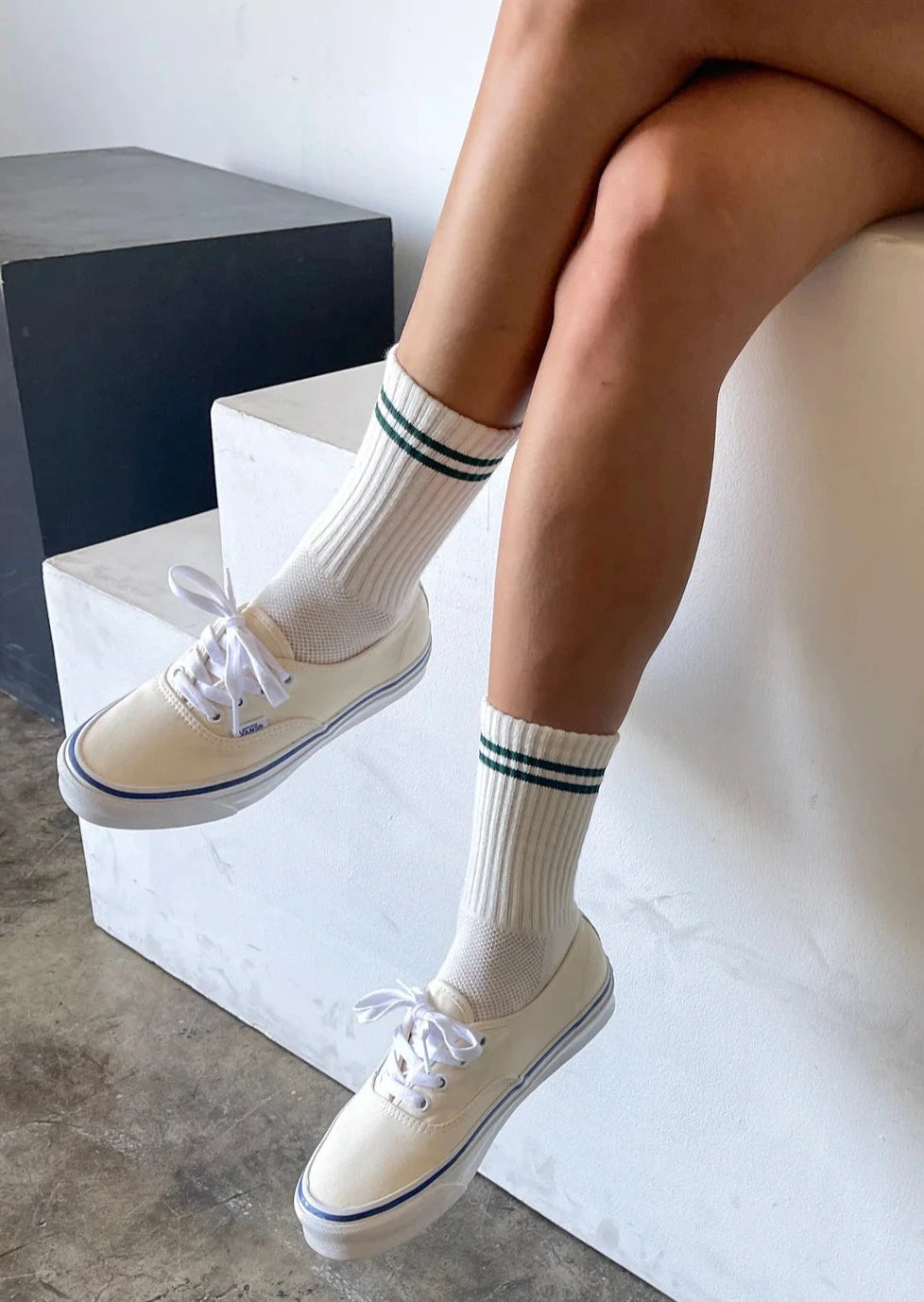 A pair of beige socks with a contrasting green double stripe on the cuffs, worn with white sneakers.
